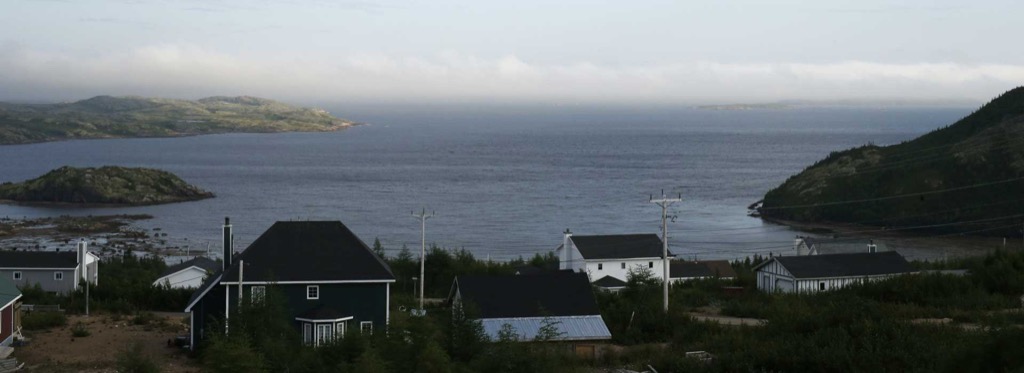 Dusk over the harbour at Bonne-Espérance, houses in the foreground and low islands
                  closing the horizon across the water.